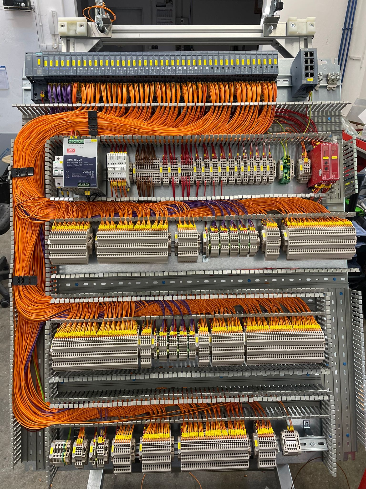 Rozbudowana szafa sterownicza z precyzyjnie ułożonymi, pomarańczowymi kablami i modułami. Widoczne liczne złącza, listwy zaciskowe i elementy automatyki.