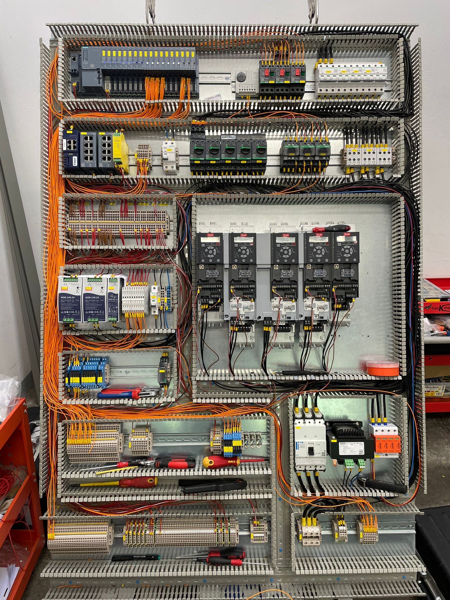Rozbudowana szafa sterownicza z licznymi modułami, przewodami i elementami elektrycznymi. Widoczne narzędzia, sugerujące etap prac instalacyjnych lub serwisowych.