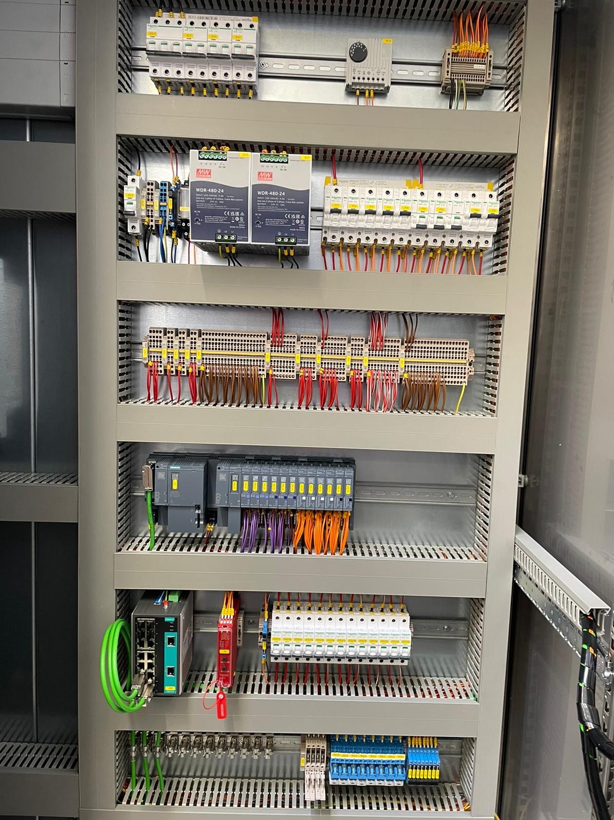 Rozdzielnica elektryczna z licznymi zabezpieczeniami, przewodami i modułami sterującymi. Widoczne elementy automatyki przemysłowej i zasilacze. Estetyczne ułożenie przewodów.