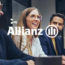 Grupa uśmiechniętych osób w biurze, z laptopami i logo Allianz, sugerująca spotkanie biznesowe lub szkolenie z zakresu ubezpieczeń.