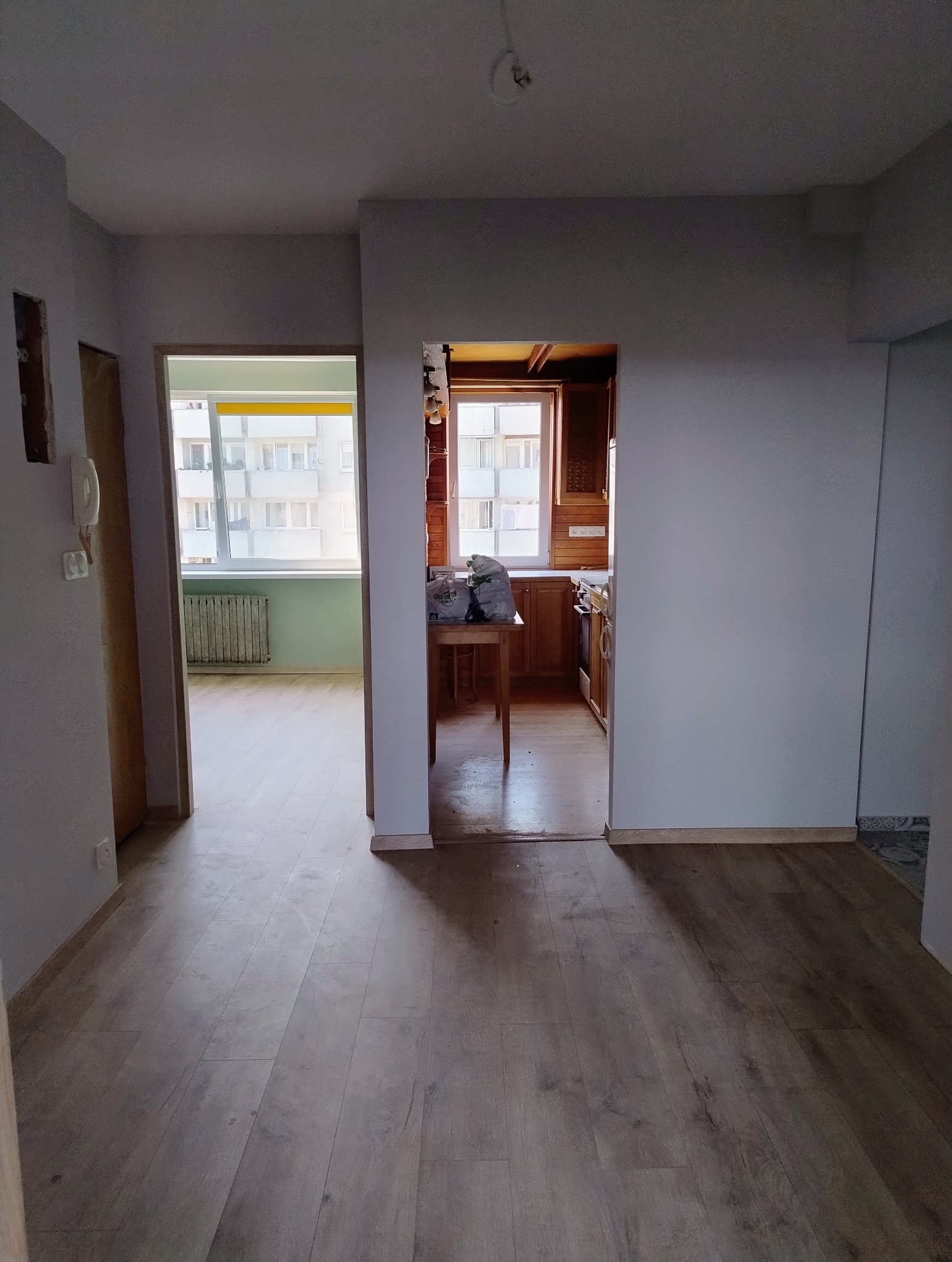 Wnętrze mieszkania po remoncie: parkiet, świeżo pomalowane ściany w odcieniach szarości, widok na pokój i kuchnię. Neutralne światło dzienne.