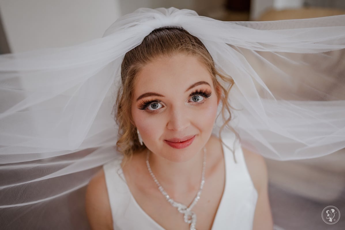 Portret panny młodej w welonie, z delikatnym makijażem i srebrną biżuterią. Ujęcie z dołu podkreśla jej spojrzenie i subtelny uśmiech.