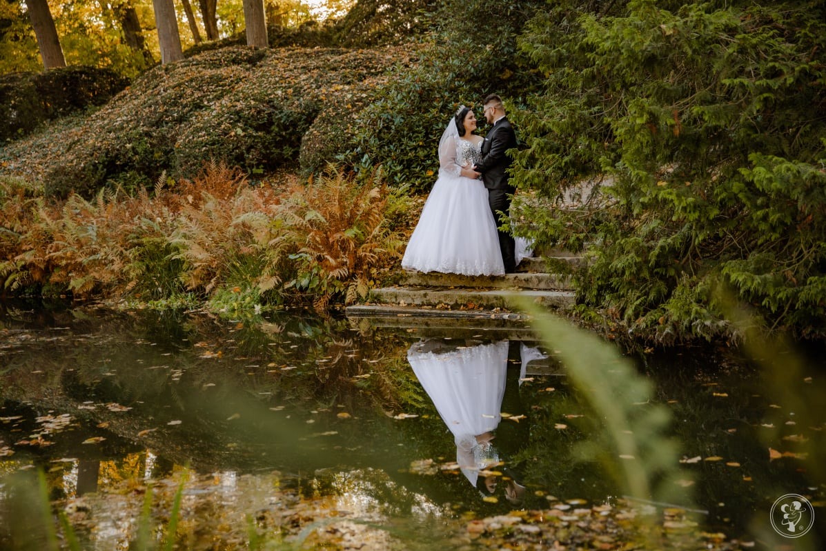 Elegancka para młoda w jesiennej scenerii parku, odbicie w wodzie dodaje głębi. Panna młoda w białej sukni, pan młody w czarnym garniturze, subtelne oświetlenie.