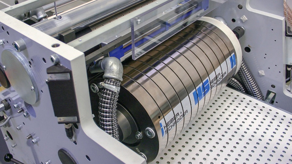 Maszyna przemysłowa Heiber + Schroder z metalowym cylindrem, widoczne elementy konstrukcyjne i przewody, perforowana podstawa.