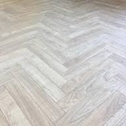 FIX&BAU Interiors VASYL CHEKAN - Jasna, drewnopodobna podłoga ułożona we wzór jodełki francuskiej, z widocznym fragmentem ciemnoniebieskiej ściany w tle, podkreślająca nowoczesny charakter wnętrza.