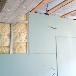 FIX&BAU Interiors VASYL CHEKAN - Montaż płyt karton-gips na metalowym stelażu z widoczną izolacją z wełny mineralnej. Częściowo wykończona ściana, widoczne kable. Prace wykończeniowe.