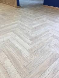 Jasna, drewnopodobna podłoga ułożona we wzór jodełki francuskiej, z widocznym fragmentem ciemnoniebieskiej ściany w tle, podkreślająca nowoczesny charakter wnętrza.