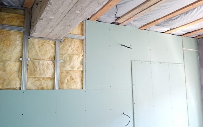 Montaż płyt karton-gips na metalowym stelażu z widoczną izolacją z wełny mineralnej. Częściowo wykończona ściana, widoczne kable. Prace wykończeniowe.