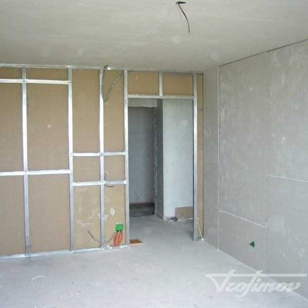 Montaż ścianki działowej z płyt karton-gips na metalowym stelażu. Widoczne przewody elektryczne i surowy stan wykończenia wnętrza.