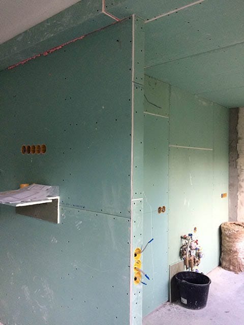 Montaż płyt gipsowo-kartonowych w łazience z widoczną instalacją wodno-kanalizacyjną i elektryczną. Widoczne profile i przygotowane otwory na gniazdka.