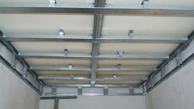 Montaż sufitu podwieszanego z płyt karton-gips na metalowej konstrukcji. Widoczne profile i elementy mocujące. Prace wykończeniowe w pomieszczeniu.