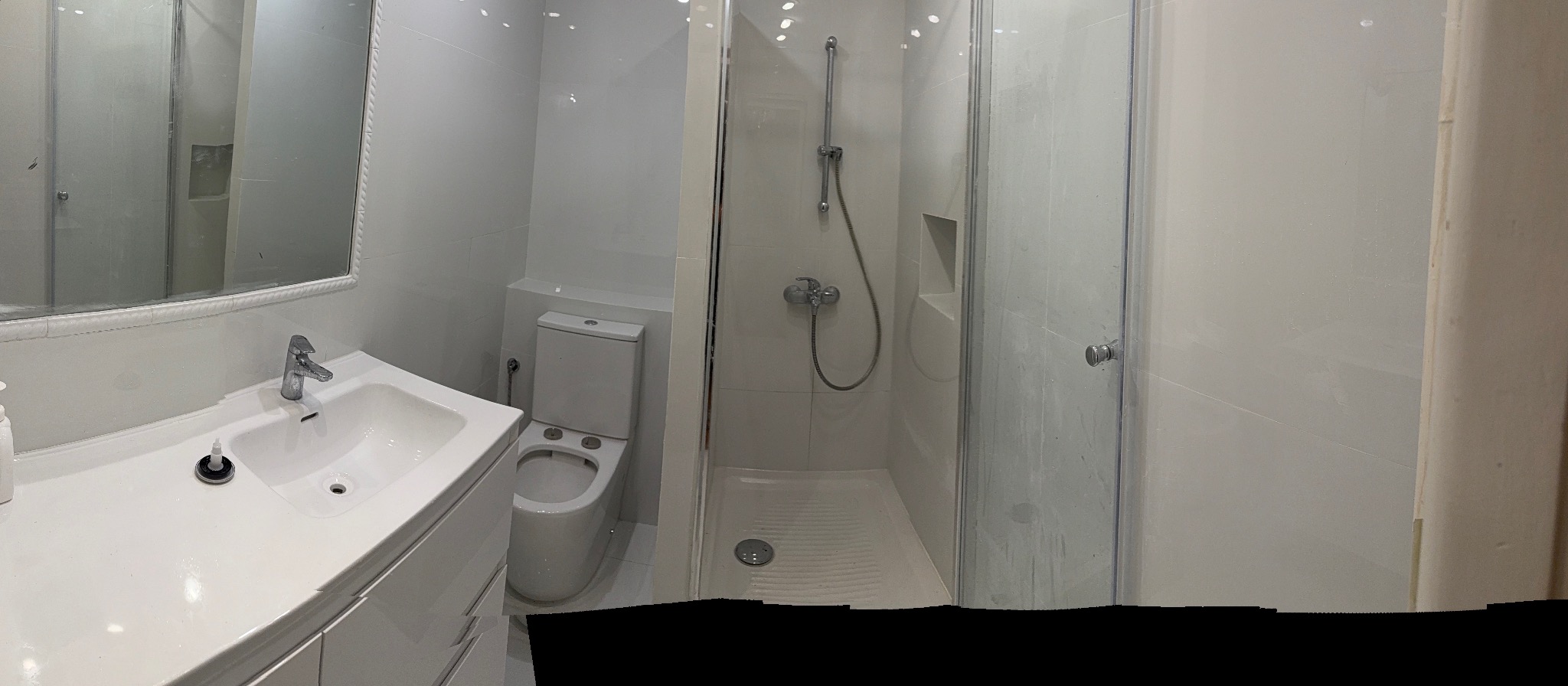 Biała, nowoczesna łazienka z kabiną prysznicową, umywalką z szafką i toaletą. Minimalistyczny design, jasne płytki, chromowana armatura.