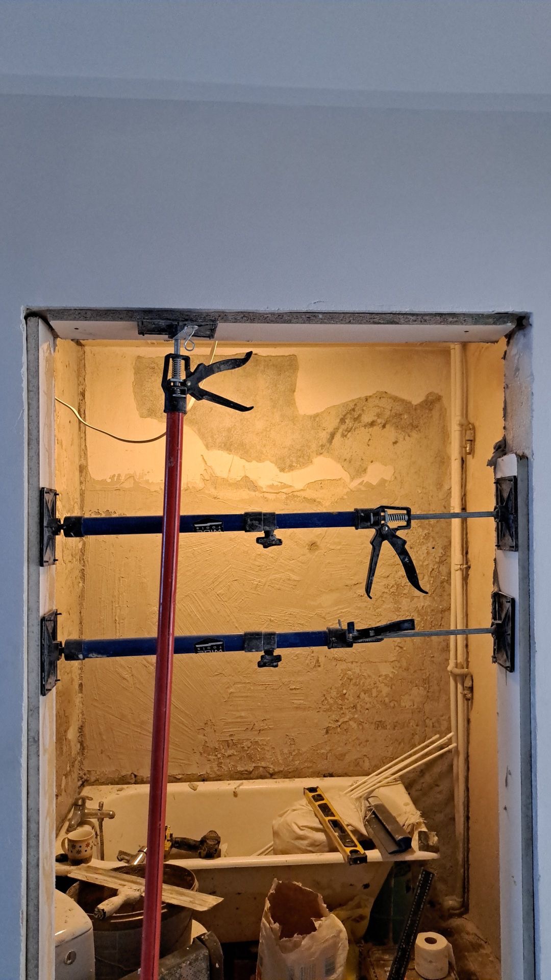 Wzmocnienie otworu drzwiowego w łazience podczas remontu. Widoczne podpory teleskopowe i przygotowana ściana do dalszych prac wykończeniowych. W tle wanna z narzędziami.