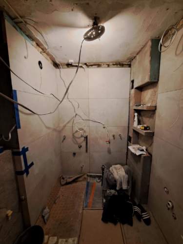 Wnętrze łazienki w trakcie remontu: widoczne płytki, instalacje elektryczne, przygotowane półki i elementy wyposażenia. Ujęcie z góry, surowe wykończenie.