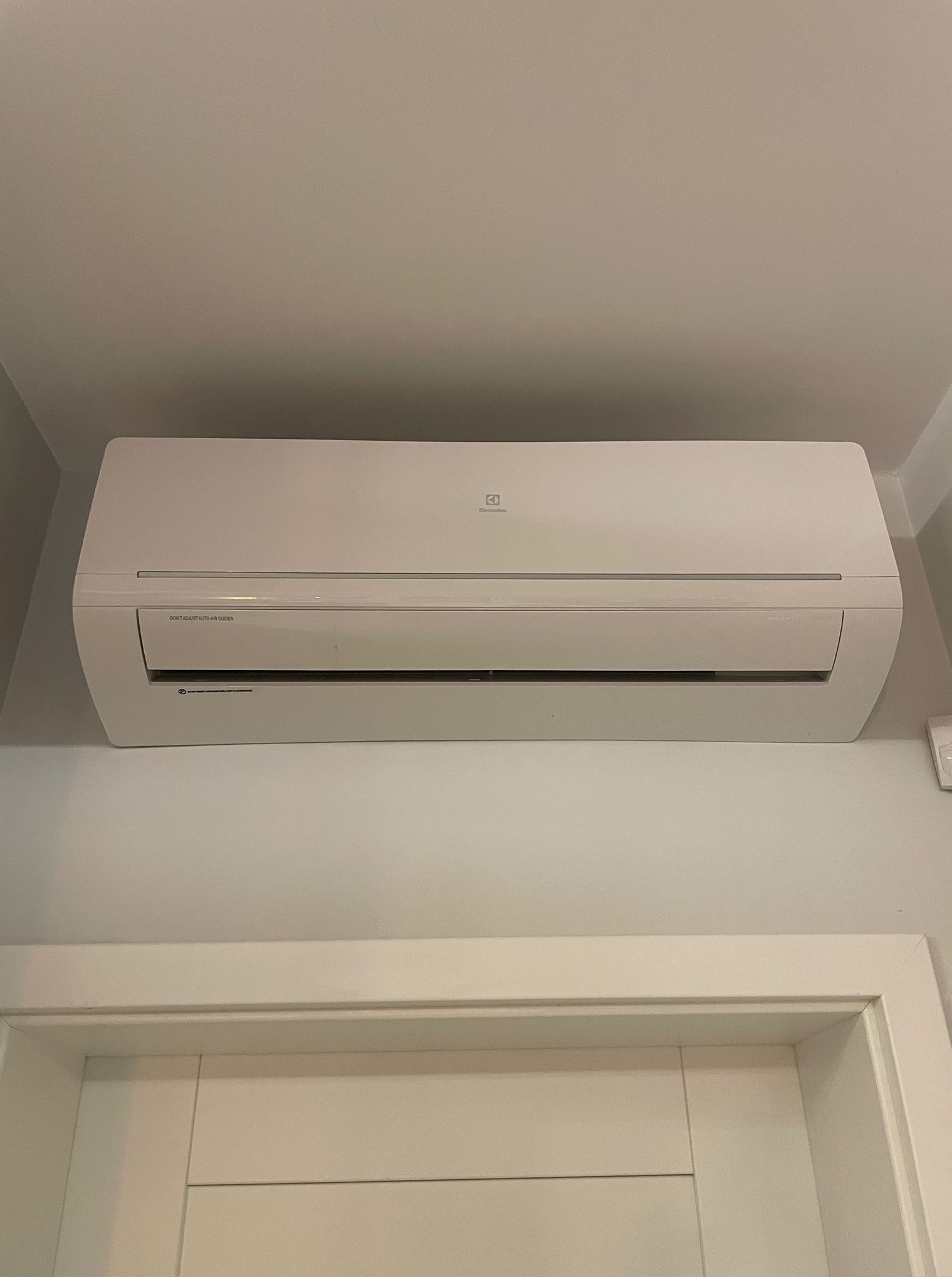 Biała klimatyzacja Electrolux zamontowana nad drzwiami w jasnym pomieszczeniu. Widoczne napisy na urządzeniu.