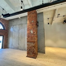 DOLIŃSKI BUDOWNICTWO DAWID DOLIŃSKI - Surowe wnętrze loftu z drewnianą podłogą, ceglanym filarem i betonową ścianą. Widoczne instalacje pod sufitem i okno z łukiem. Minimalistyczny design.