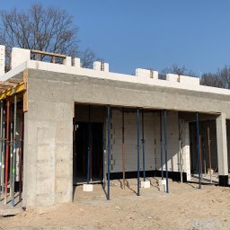 DOLIŃSKI BUDOWNICTWO DAWID DOLIŃSKI - Budowa domu z betonu komórkowego w trakcie realizacji. Widoczne szalunki i podpory. Częściowo otynkowane ściany. W tle drzewa i błękitne niebo.