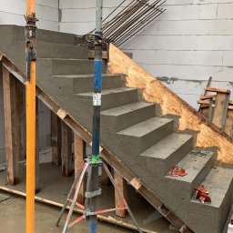 DOLIŃSKI BUDOWNICTWO DAWID DOLIŃSKI - Betonowe schody w trakcie budowy, widoczne szalunki i podpory. Ściany z bloczków betonowych, zbrojenie w tle. Etap wylewania betonu na schody.