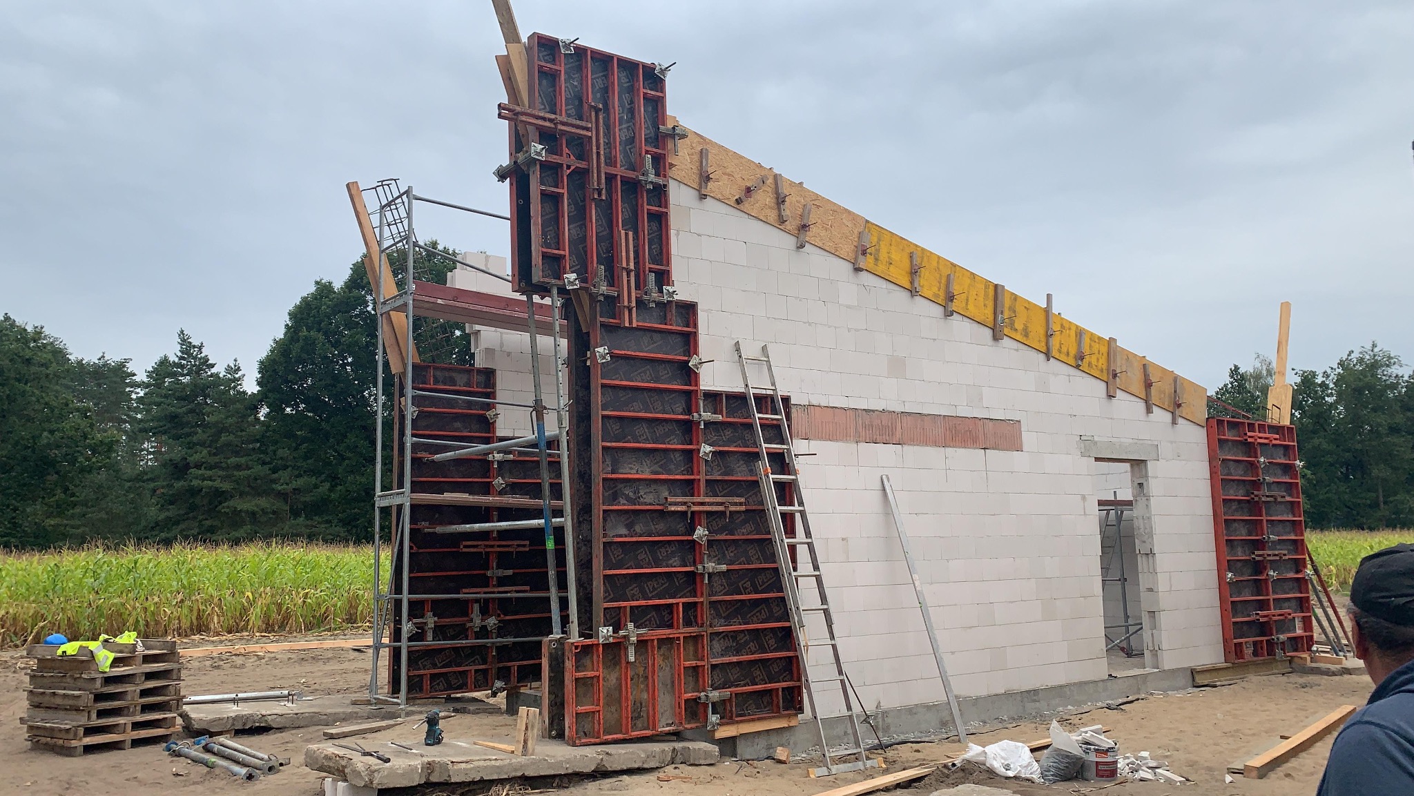 Wznoszenie ścian z bloczków betonu komórkowego z użyciem szalunków systemowych. Widoczne rusztowania i elementy konstrukcyjne. Budowa domu w trakcie realizacji.