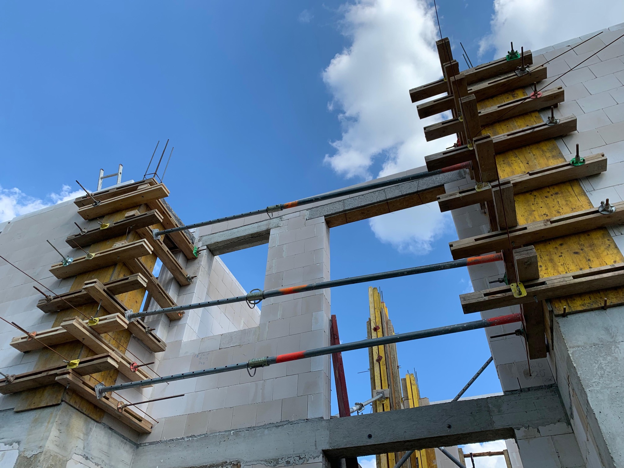 Wznoszenie ścian z betonu komórkowego Ytong z użyciem szalunków i podpór. Widok na fragment budynku w trakcie budowy, błękitne niebo w tle.