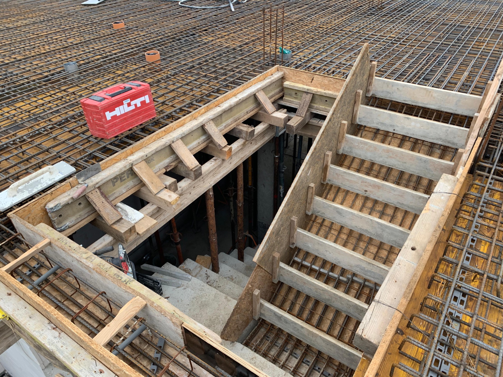 Zbrojenie stropu z otworem na schody, drewniane szalunki, widoczna skrzynka narzędziowa Hilti. Detal budowy budynku żelbetowego z perspektywy góry.