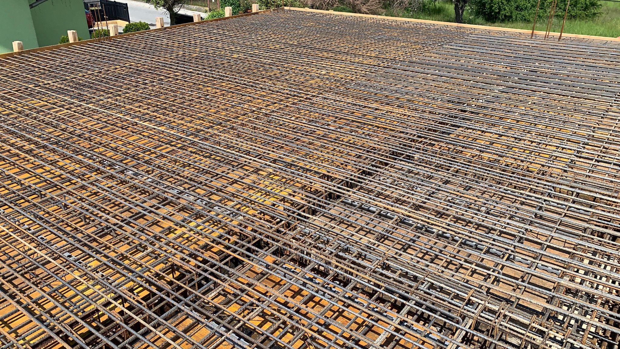 Siatka zbrojeniowa ułożona na drewnianym szalunku, przygotowana do zalania betonem. Widok z góry, regularny układ prętów, elementy drewniane w tle.