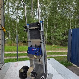 Fast&Best Marcin Kucio - Wózek schodowy elektryczny ETS20 na platformie załadunkowej, z widocznym lasem w tle. Urządzenie gotowe do transportu towarów po schodach.