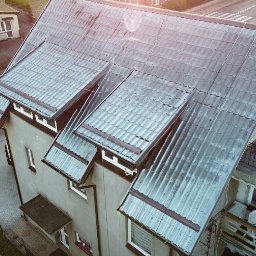 MAL-BAU WOŹNICA, KOWALCZYK SPÓŁKA CYWILNA - Zdjęcie z góry przedstawia dom z szarą dachówką i oknami. Dach jest częściowo pokryty mchem i wymaga czyszczenia. Widoczna ulica i inne budynki w tle.