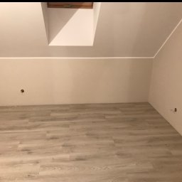 Sebastian Tramś Usługi remontowo-wykończeniowe - Poddasze po remoncie: jasne panele podłogowe, świeżo pomalowane ściany w odcieniach beżu, okno dachowe, widoczne puszki elektryczne. Częściowo widoczna ściana z cegły.