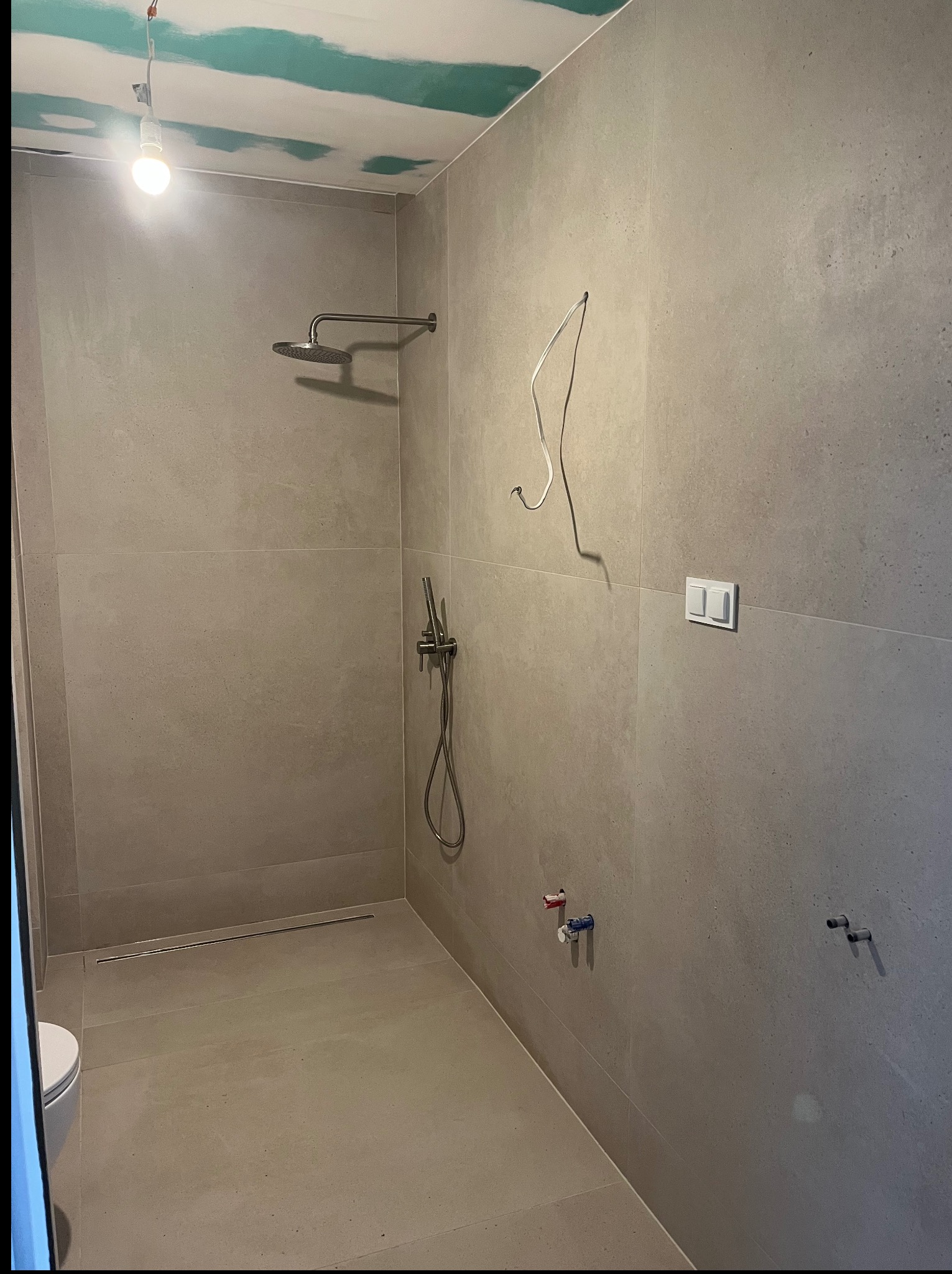 Łazienka w trakcie remontu: szara, matowa glazura, sufit z płyt gips-karton z widocznymi łączeniami, instalacja prysznicowa, odpływ liniowy w podłodze.