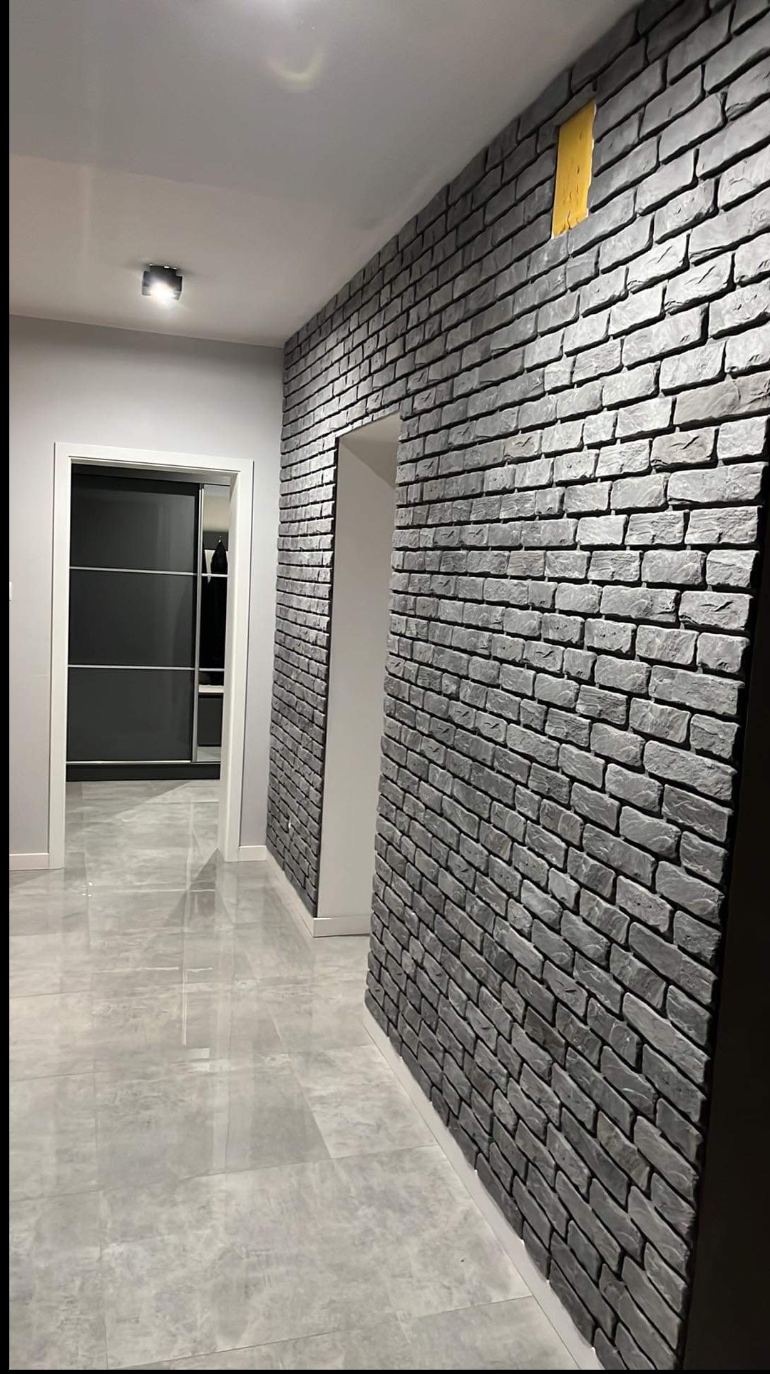 Korytarz z szarą cegłą dekoracyjną na ścianie i błyszczącą, szarą podłogą. Widoczne drzwi przesuwne do garderoby.