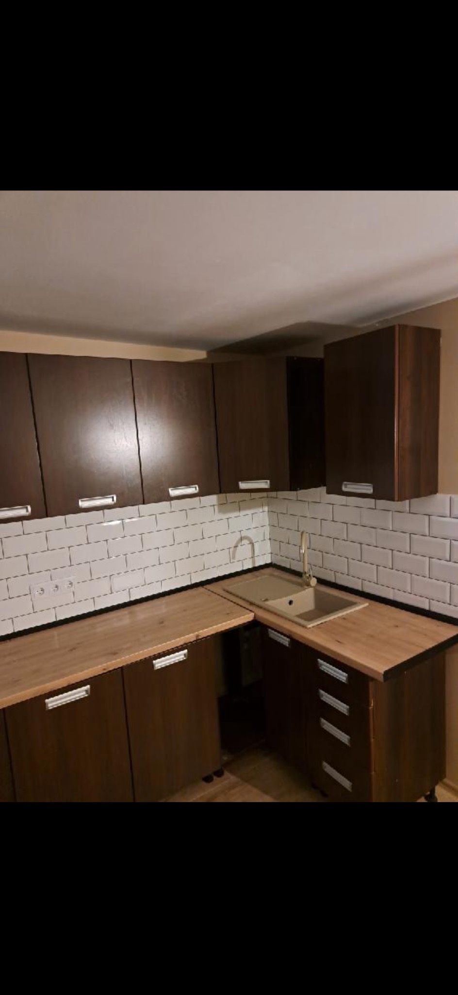 Nowoczesna kuchnia z brązowymi szafkami, drewnianym blatem i białymi płytkami imitującymi cegłę. Bateria kuchenna i zlewozmywak w odcieniach beżu.