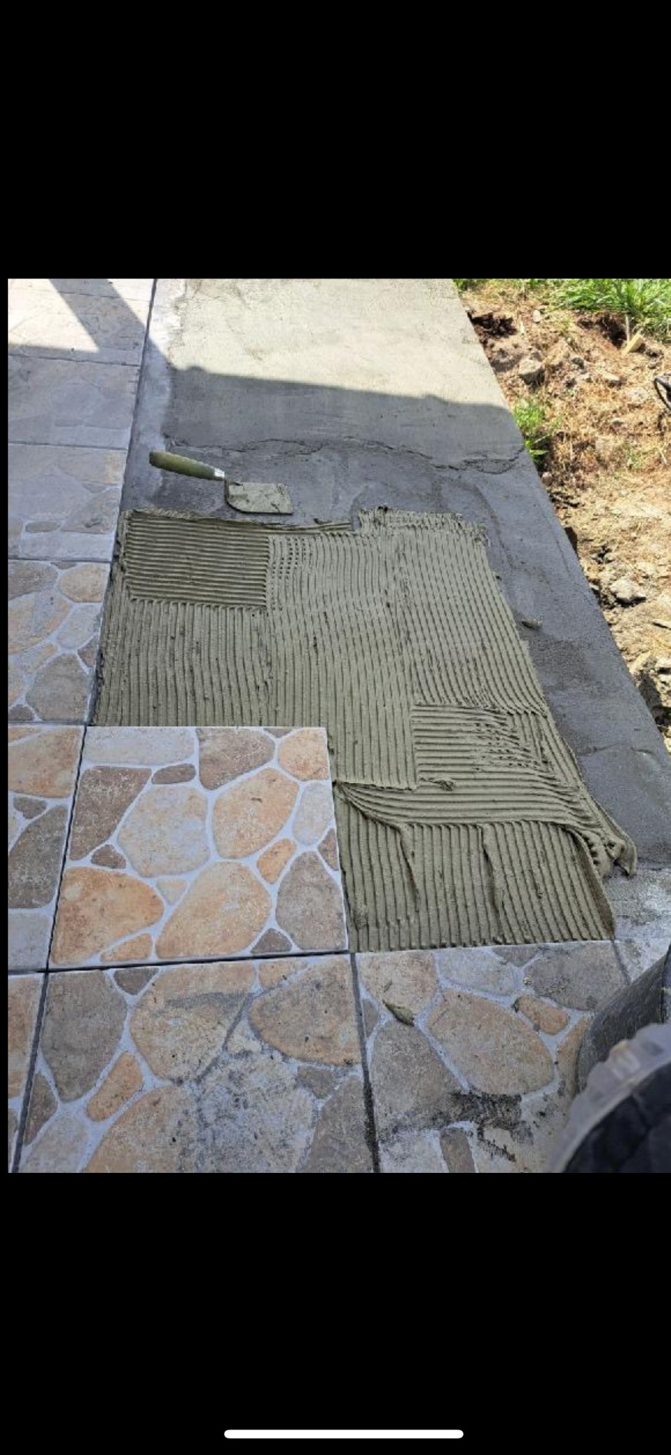 Układanie mozaiki z kamieni na zewnątrz. Widoczna zaprawa i szpachelka. Częściowo ułożona podłoga z mozaiki. Prace wykończeniowe na balkonie.