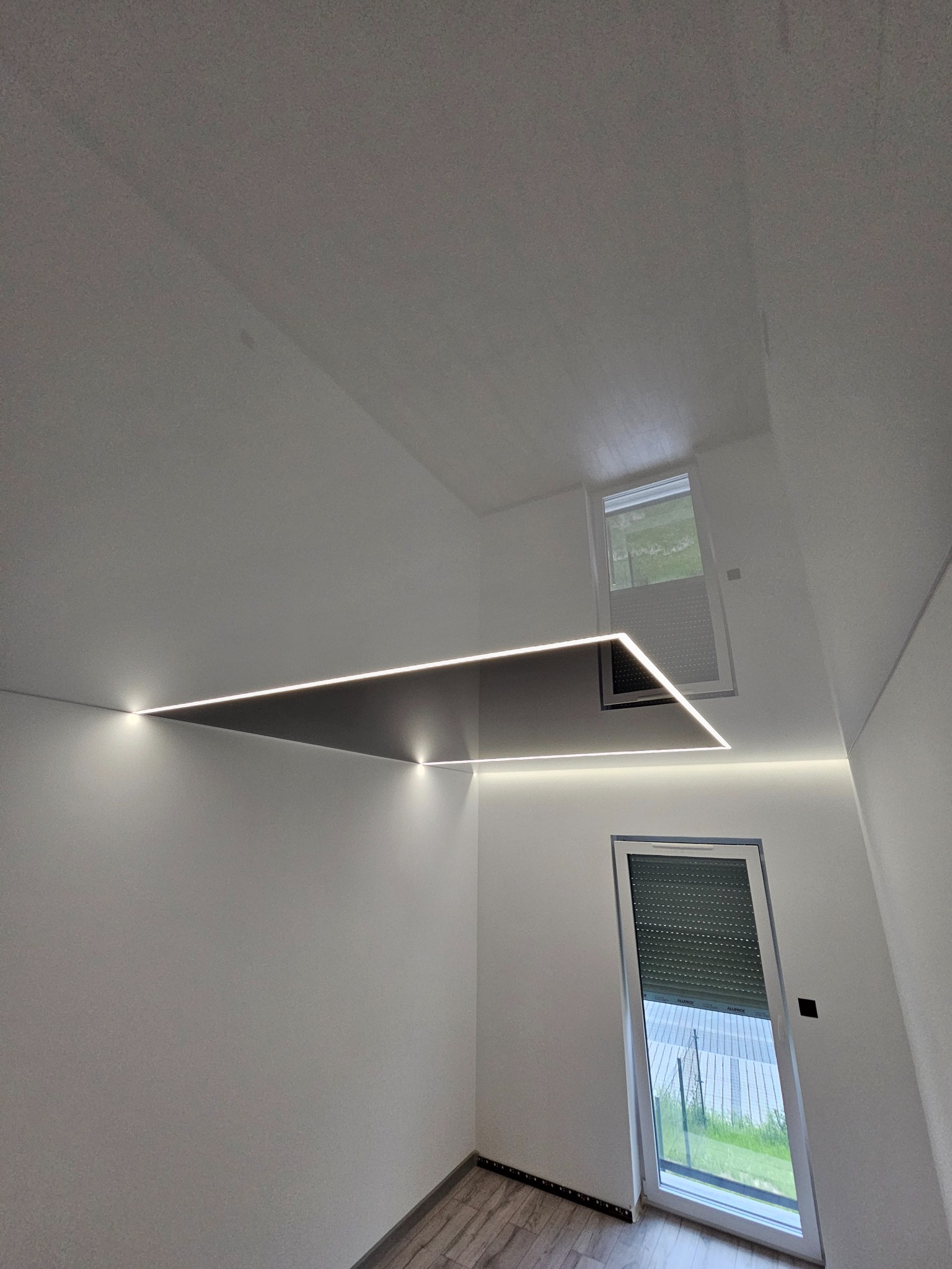 Nowoczesny sufit z podwieszaną konstrukcją i liniowym oświetleniem LED w jasnym wnętrzu z oknami i drewnopodobną podłogą. Minimalistyczny design.