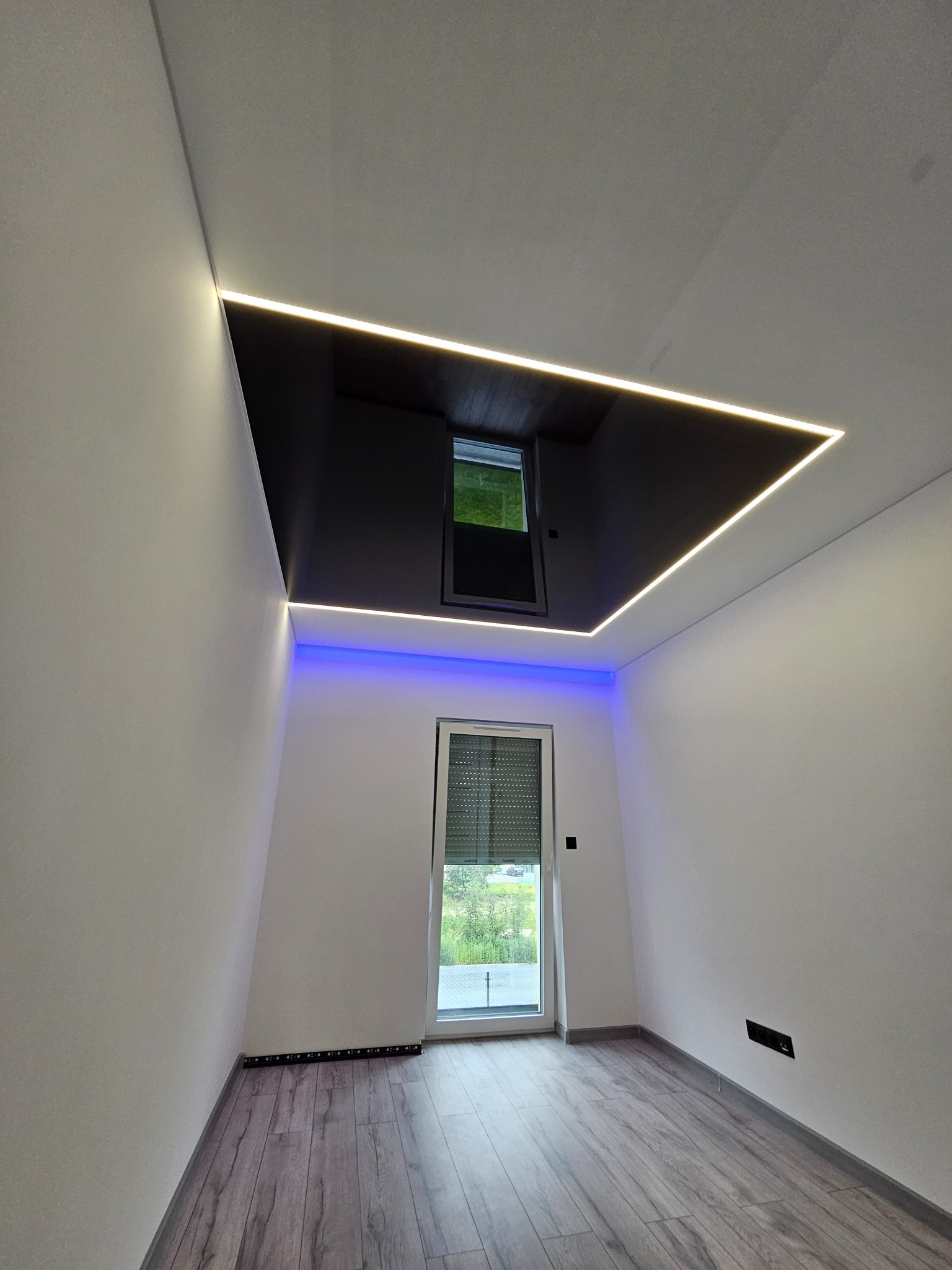 Nowoczesne wnętrze z czarnym sufitem podwieszanym, oświetleniem LED i drewnianą podłogą. Okno z roletami wpuszcza naturalne światło.