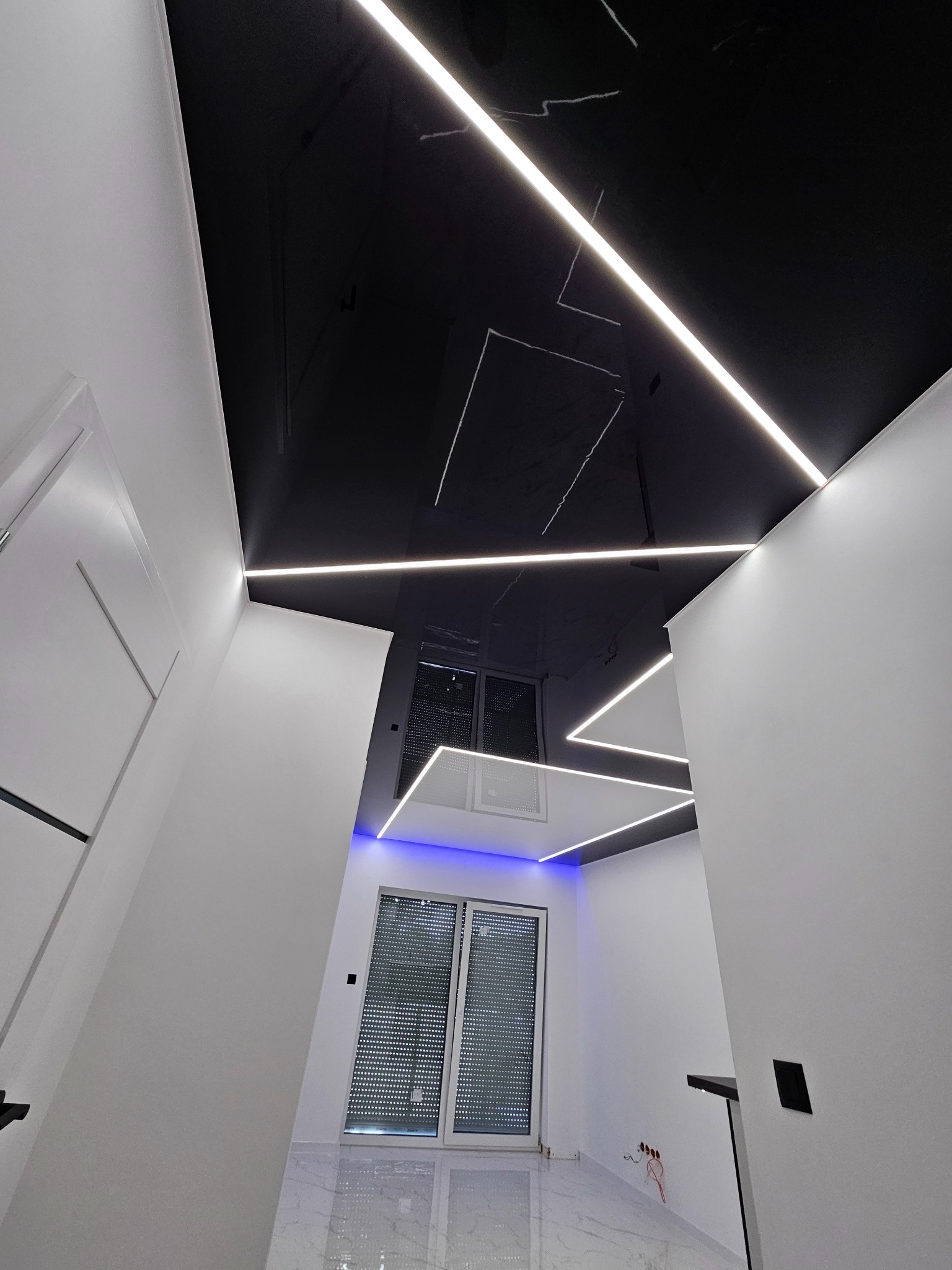 Nowoczesny sufit napinany z czarnym połyskiem i oświetleniem LED w kształcie linii, widok z dołu, podkreślający minimalistyczny design wnętrza.