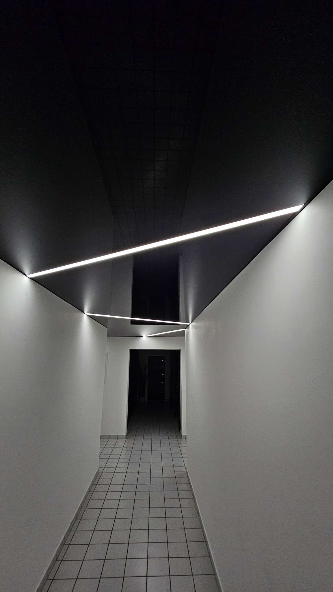 Korytarz z czarnym, błyszczącym sufitem napinanym i liniowym oświetleniem LED. Widok w perspektywie, podkreślający nowoczesny design i minimalizm wnętrza.