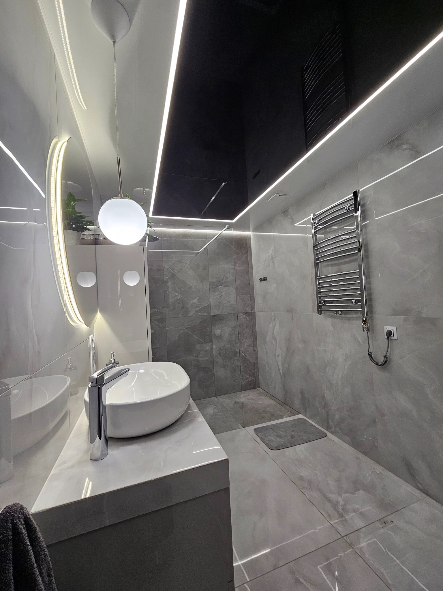 Nowoczesna łazienka w szarościach z czarnym sufitem napinanym i oświetleniem LED. Umywalka nablatowa, lustro z podświetleniem i grzejnik drabinkowy.