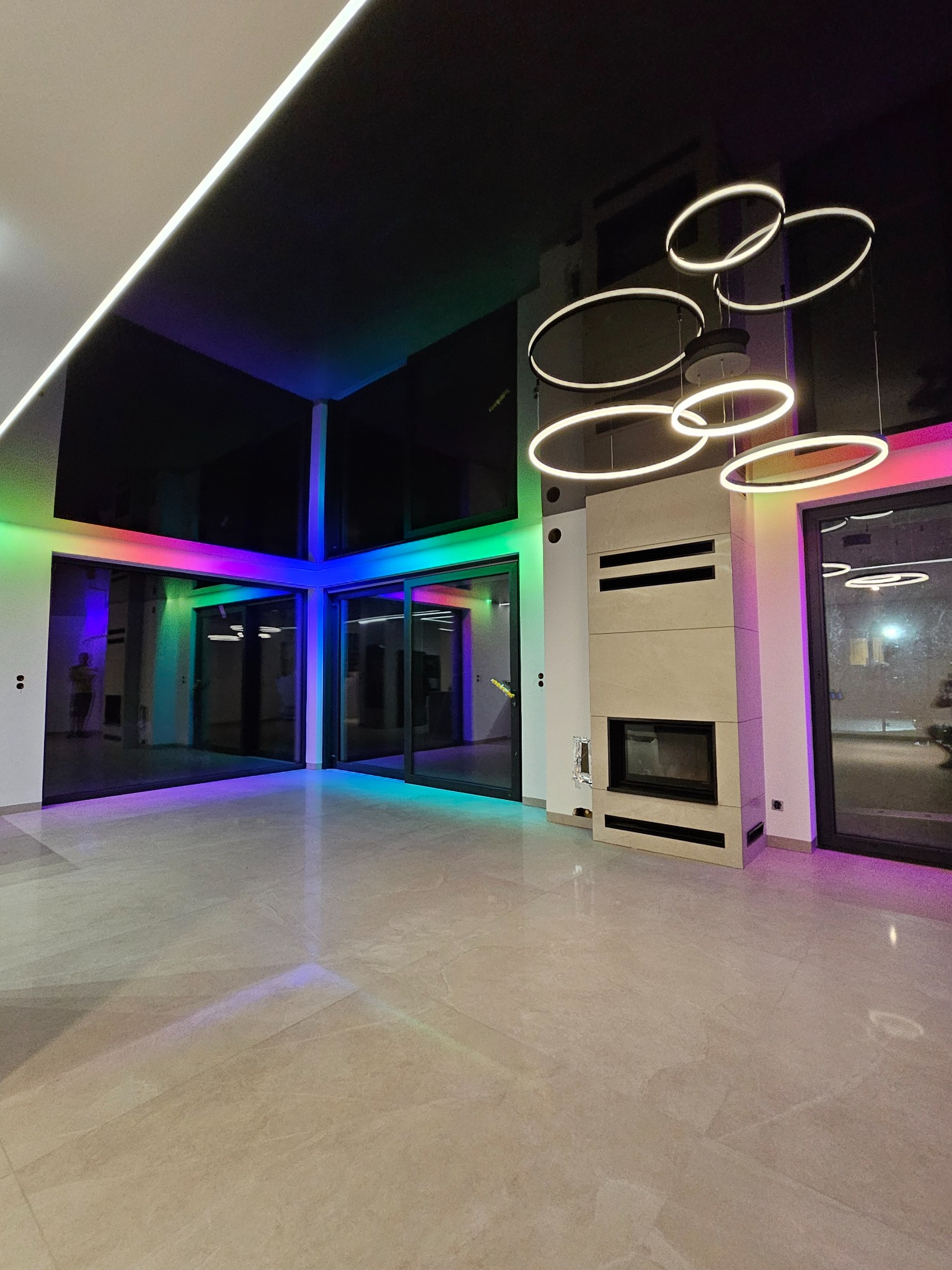 Nowoczesne wnętrze z czarnym sufitem napinanym i oświetleniem LED RGB wzdłuż okien. Okrągłe lampy wiszące nad kominkiem. Minimalistyczny design.