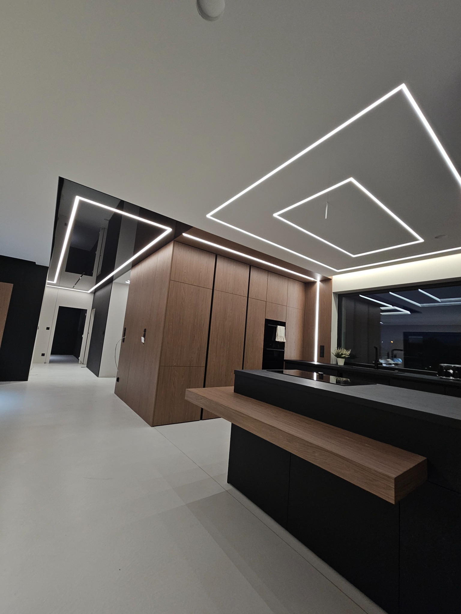 Nowoczesne wnętrze z oświetleniem LED w kształcie kwadratów na suficie, drewniane szafy i czarne elementy wykończenia, minimalistyczny design.