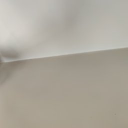 Maltop - Gładzie I Malowanie - Ręka w roboczej rękawicy precyzyjnie wykańczająca gładkie połączenie jasnej ściany z białym sufitem, tworząc czystą linię narożnika.