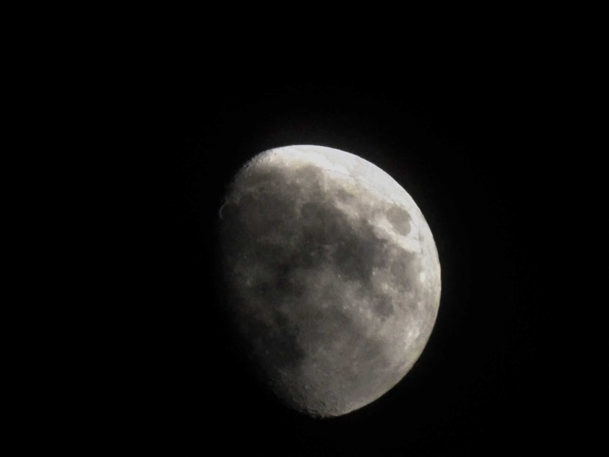 Szary, blady księżyc w fazie zbliżającej się do pełni, widoczny na czarnym tle nocnego nieba. Szczegółowa faktura powierzchni z kraterami i nierównościami.