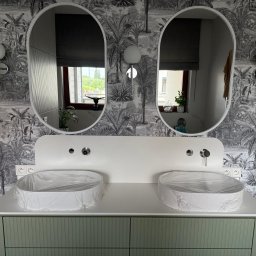 Masters - Nowoczesna łazienka z podwójną umywalką i lustrami owalnymi na tle tapety w tropikalne wzory. Umywalki zabezpieczone folią ochronną, zielona szafka pod umywalką.