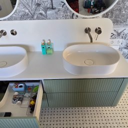 Masters - Nowoczesna łazienka z podwójną umywalką nablatową, zieloną szafką z szufladami i wzorzystą tapetą w tropikalnym stylu. Otwarta szuflada z akcesoriami.