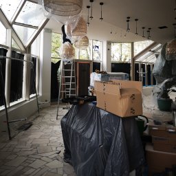 Energo-instal - Wnętrze lokalu w trakcie montażu oświetlenia: wiszące lampy w osłonach, drabina, narzędzia i kartony. Widoczne okna i przeszklony dach.