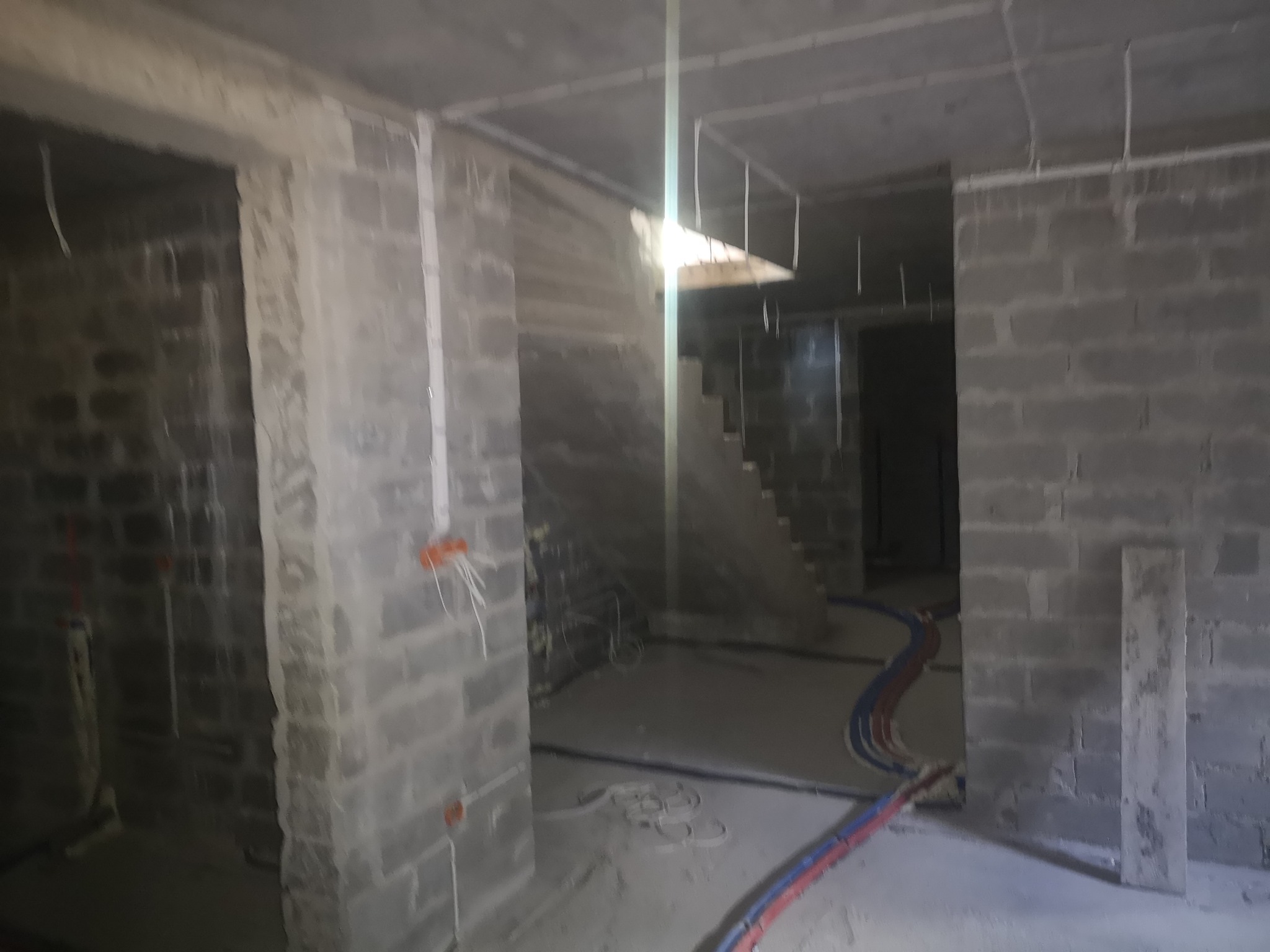 Surowy stan budynku w trakcie prac instalacyjnych: widoczne przewody elektryczne i rury, ściany z szarego betonu komórkowego, sufit z widocznymi elementami oświetlenia.