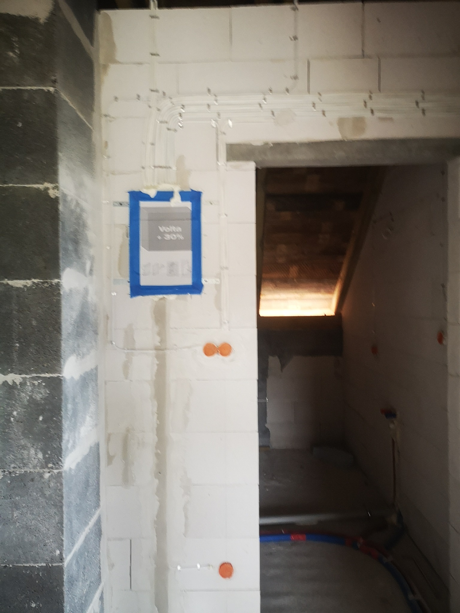 Wnętrze w trakcie prac: widoczne przewody elektryczne w białych rurkach, puszka pod tynk z naklejką, ściany z betonu komórkowego i instalacja wodna.