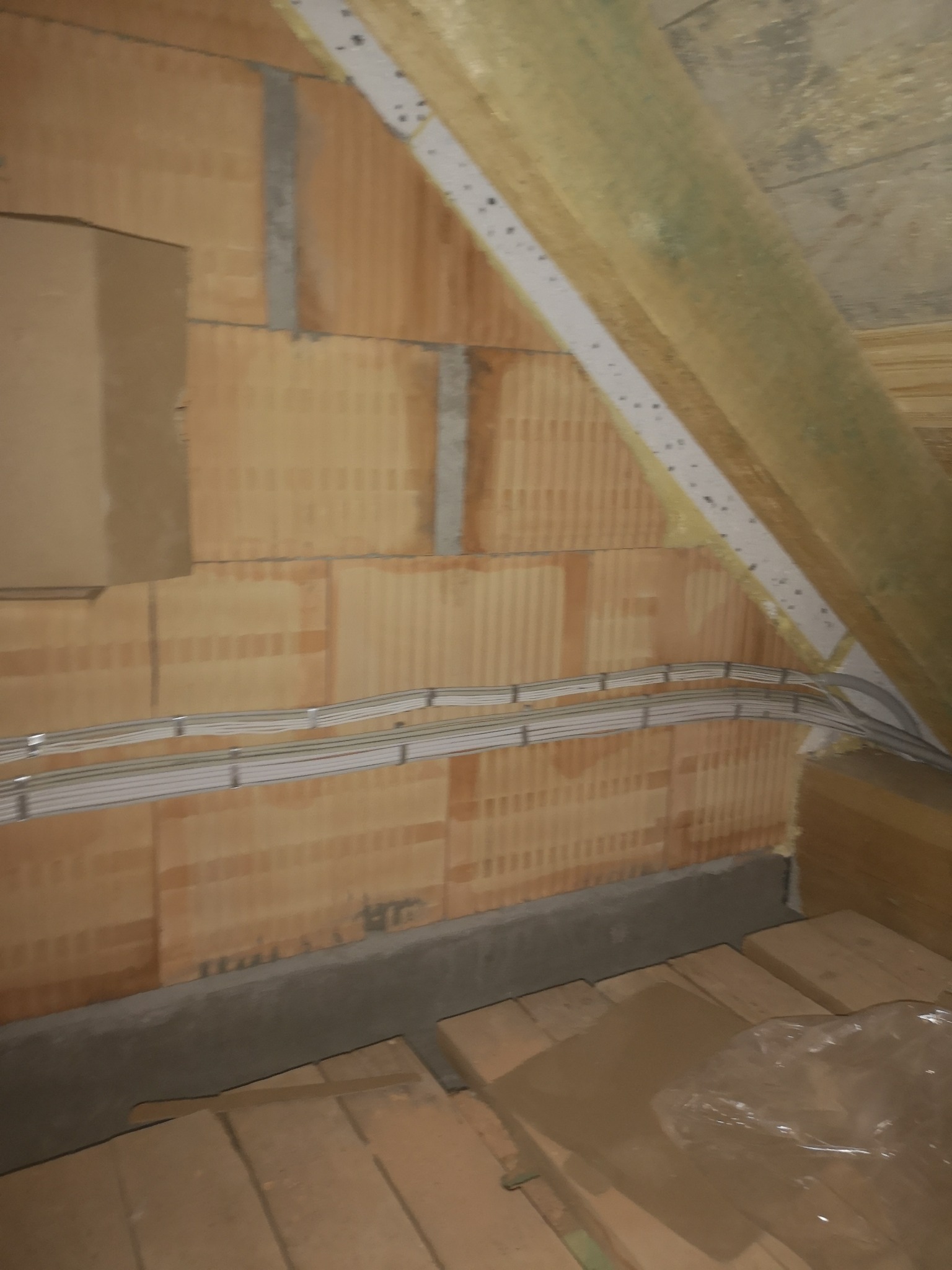 Instalacja elektryczna w trakcie prac na poddaszu w Sulęczyno. Widoczne kable prowadzone wzdłuż ściany z pustaków ceramicznych, zamocowane do metalowych uchwytów.