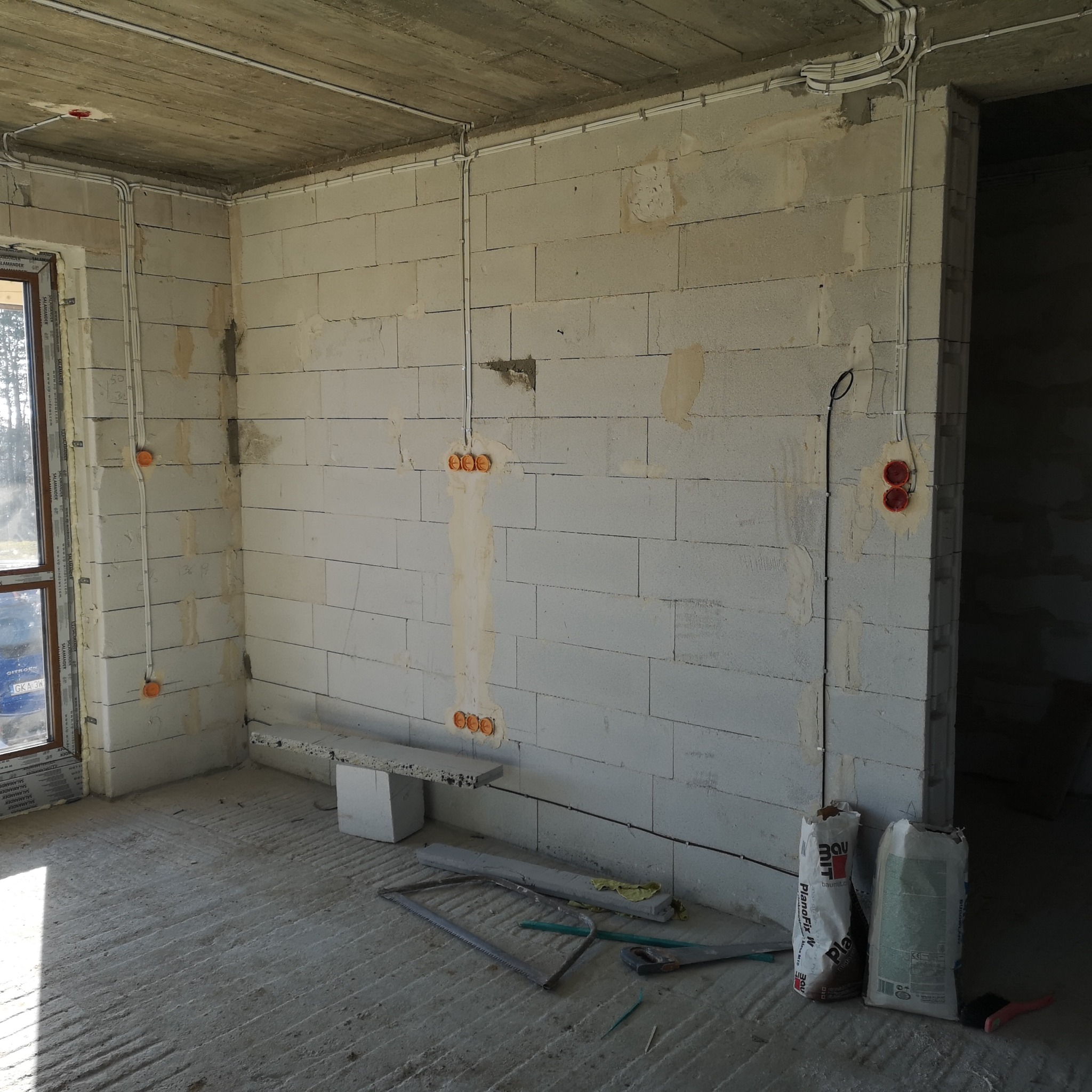 Surowy stan: widok na wnętrze w trakcie prac elektrycznych. Białe kable prowadzone po ścianach z betonu komórkowego, puszki instalacyjne w ścianach. Podłoga wylewka.