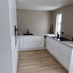 Michal Zolopa - Nowoczesna, jasna kuchnia w Opolu z białymi szafkami i drewnianą podłogą. Minimalistyczny design, czarny zlew i płyta indukcyjna. Stonowana kolorystyka ścian.